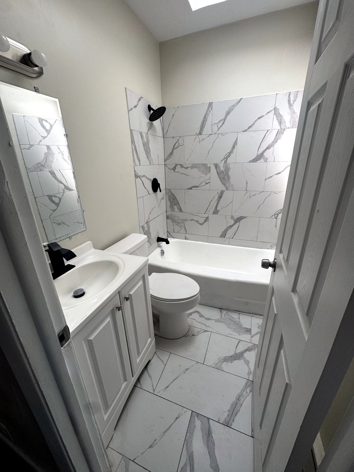 Bathroom with marble-look tile tub surround and floor, white vanity, and black fixtures