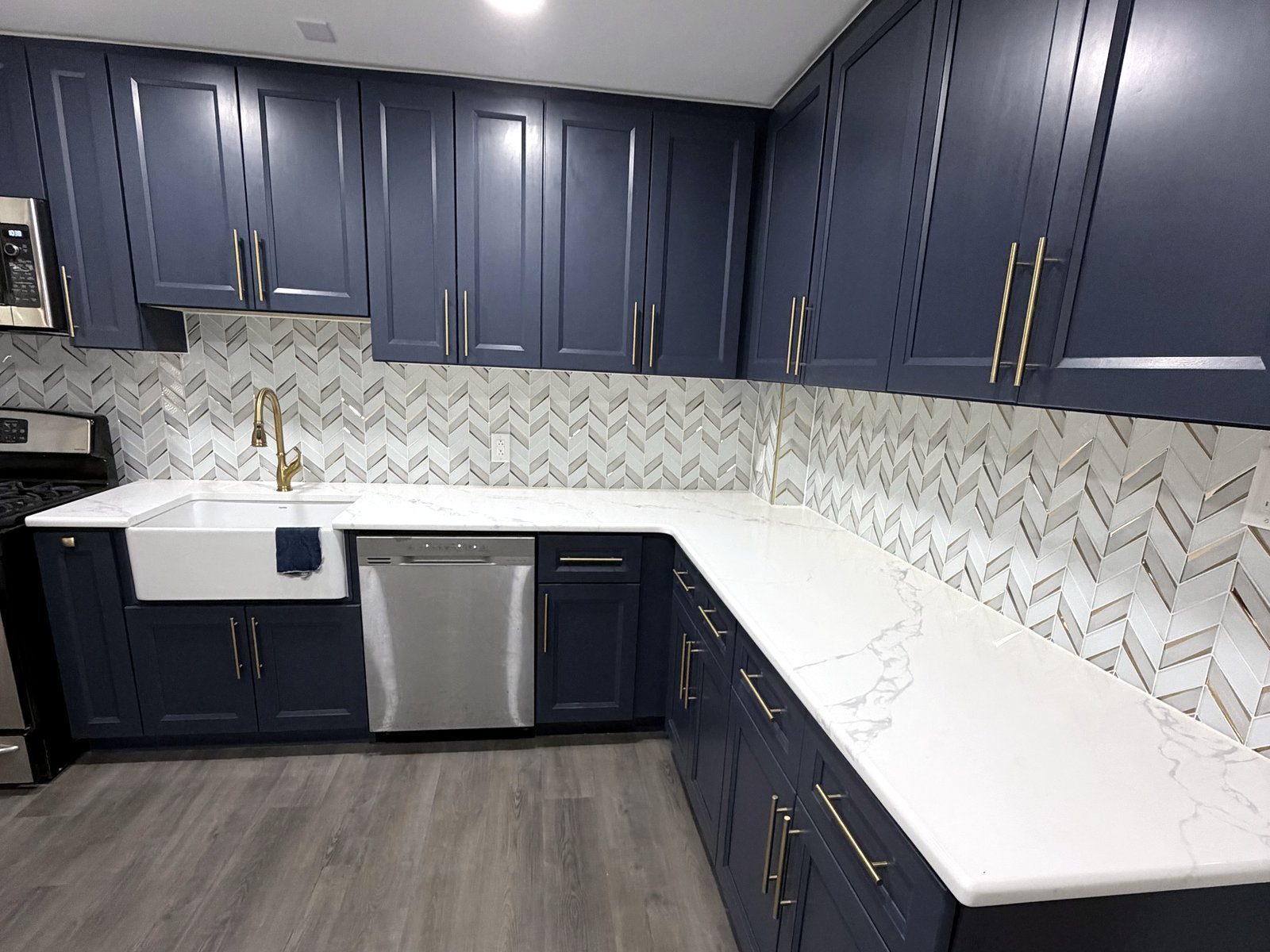 Navy cabinetry with an L-shaped quartz countertop and chevron glass tile backsplash