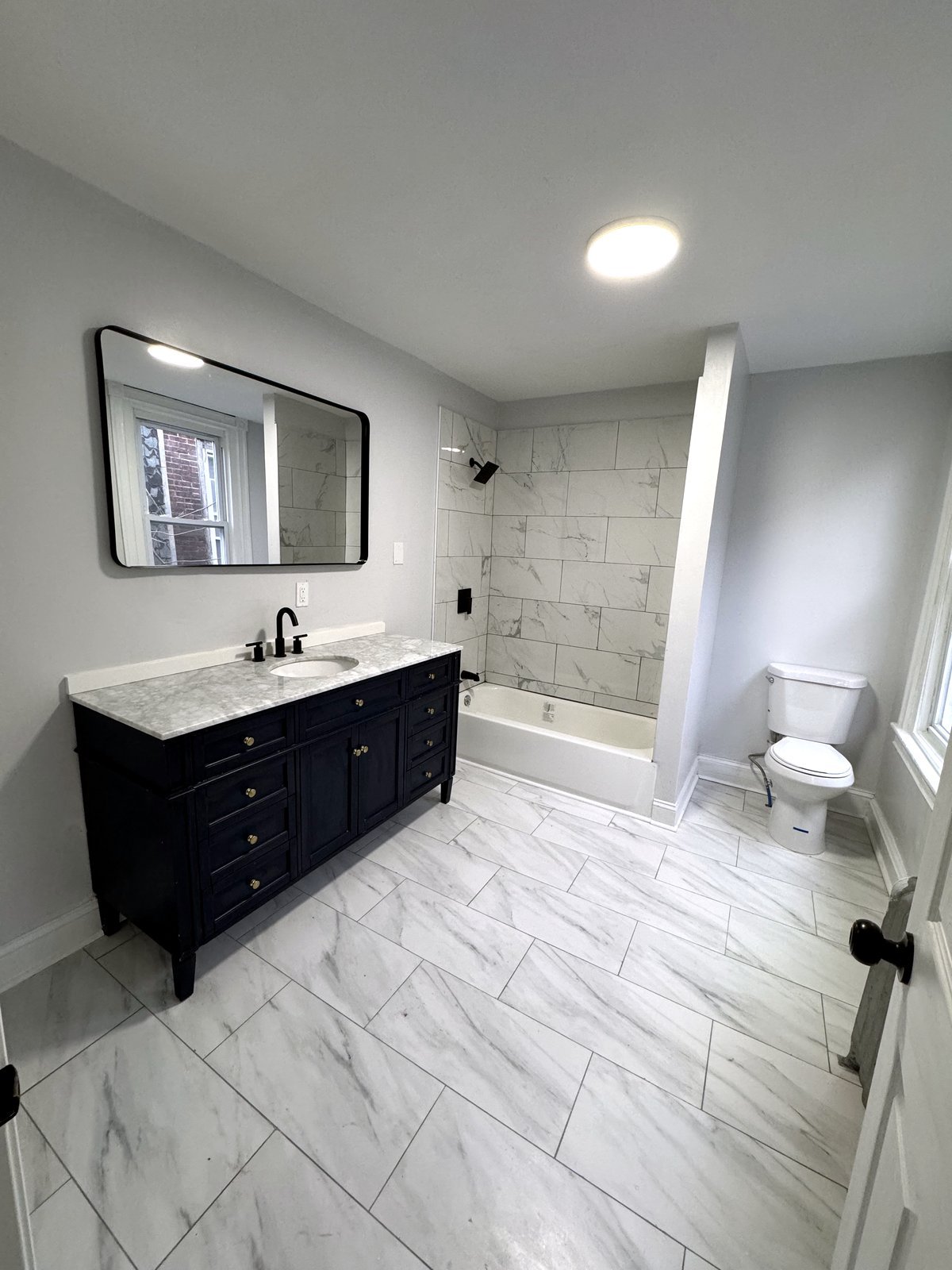 Renovated bathroom with navy vanity and marble-look tile shower surround