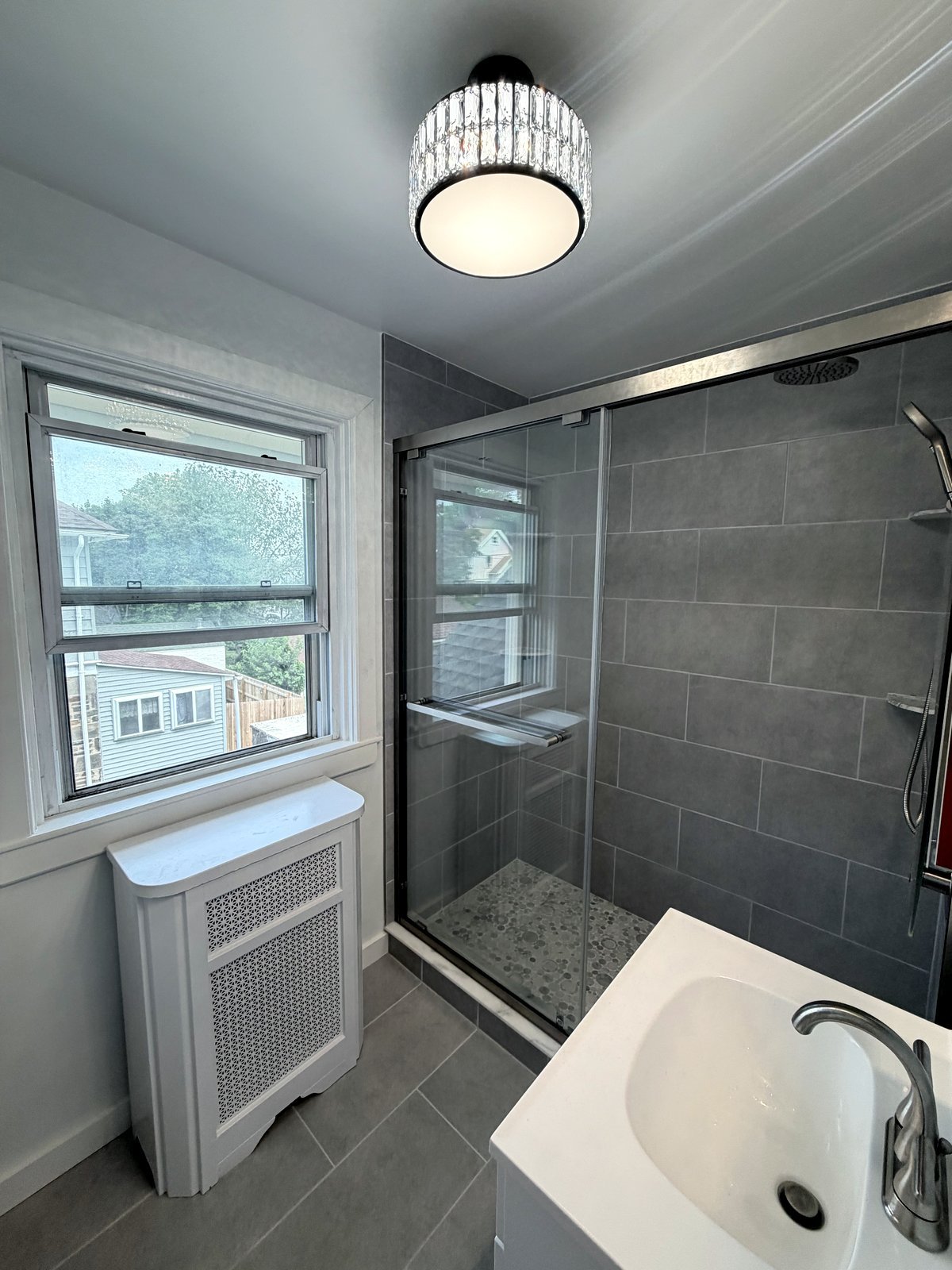 Renovated bathroom with gray tile shower, glass door, and vanity