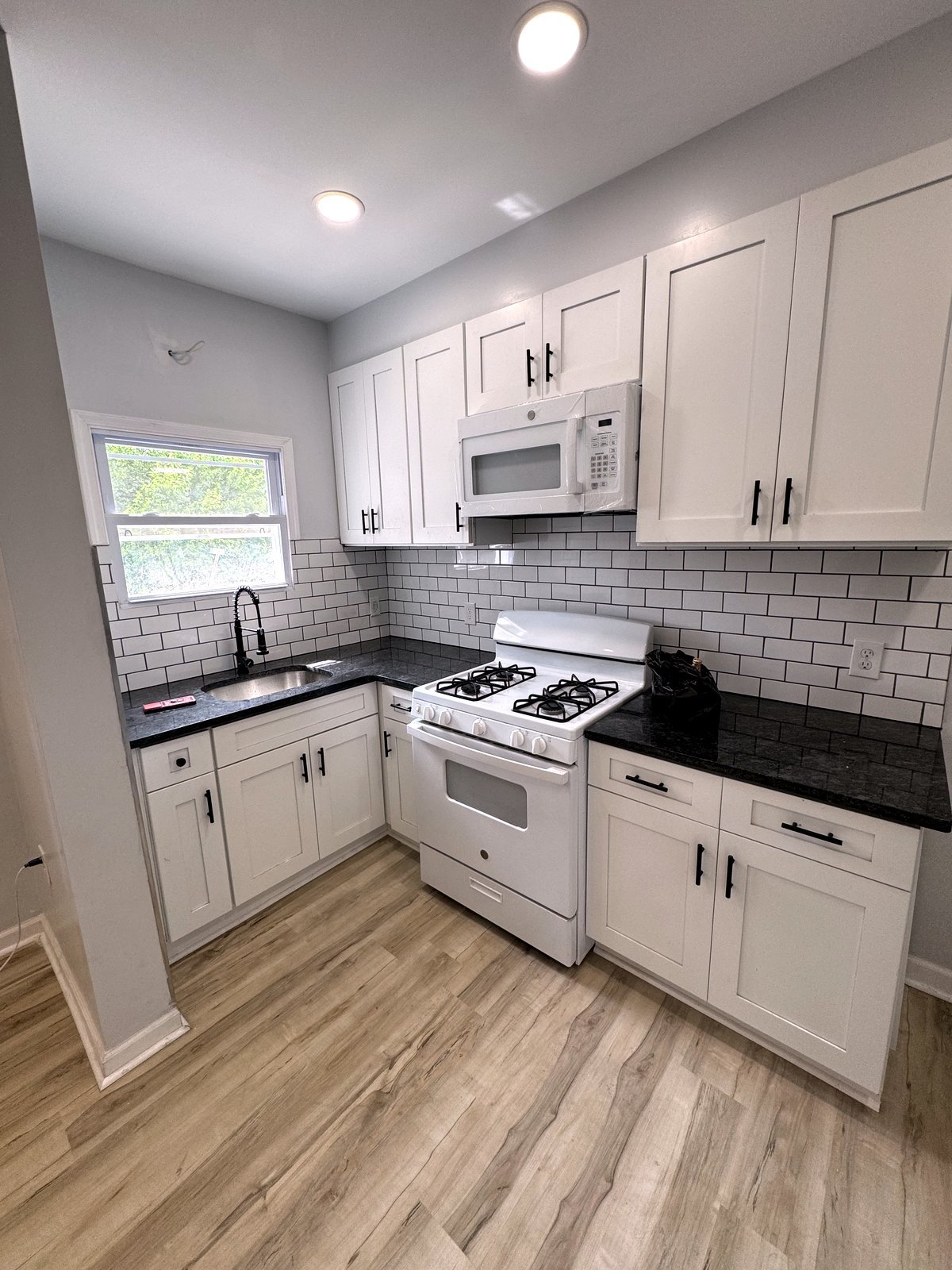 Kitchen with white shaker cabinets, subway tile backsplash, gas range, and wood-look flooring